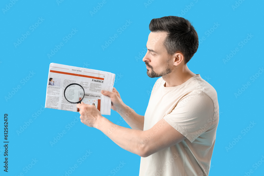 Handsome man with magnifier and newspaper on blue background