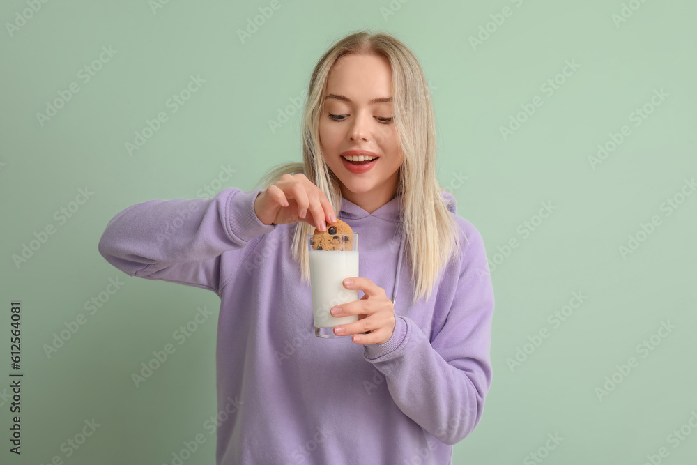 Young woman with glass of milk and cookie on green background