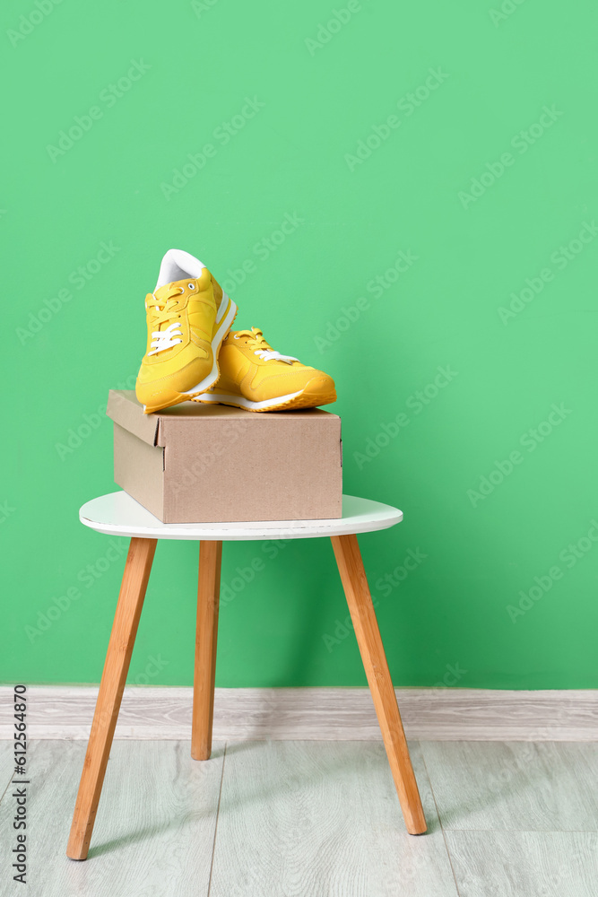 Table with cardboard box and stylish sneakers near color wall