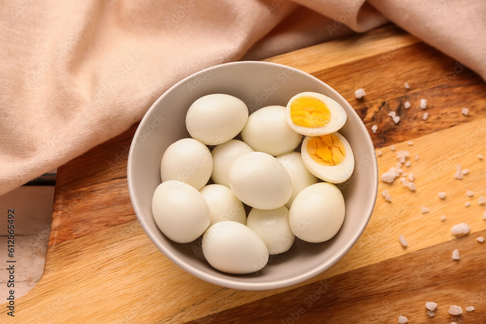 Board with bowl of boiled quail eggs and shells, closeup