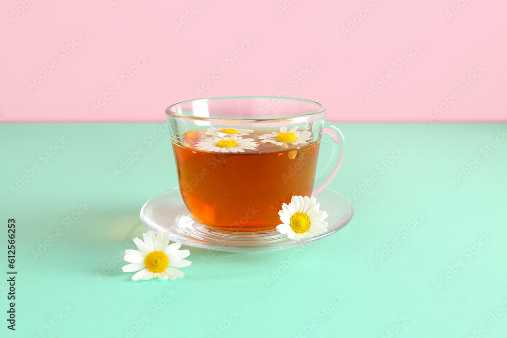 Cup of natural chamomile tea and flowers on turquoise table near pink wall