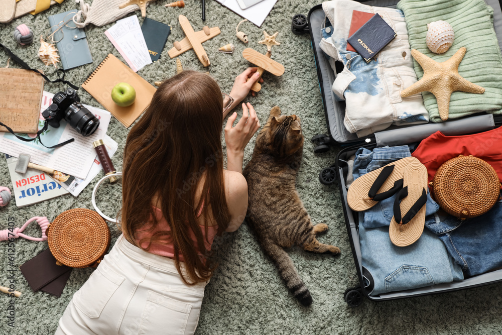 Woman with Scottish fold cat and travelling accessories on green carpet, top view