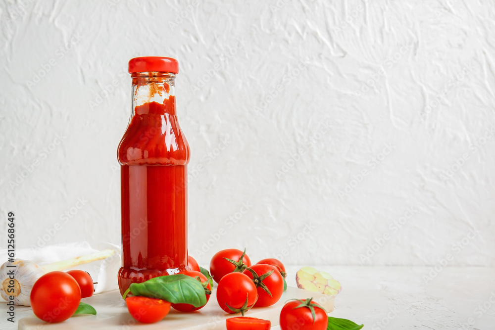 Board with glass bottle of ketchup and tomatoes on white background