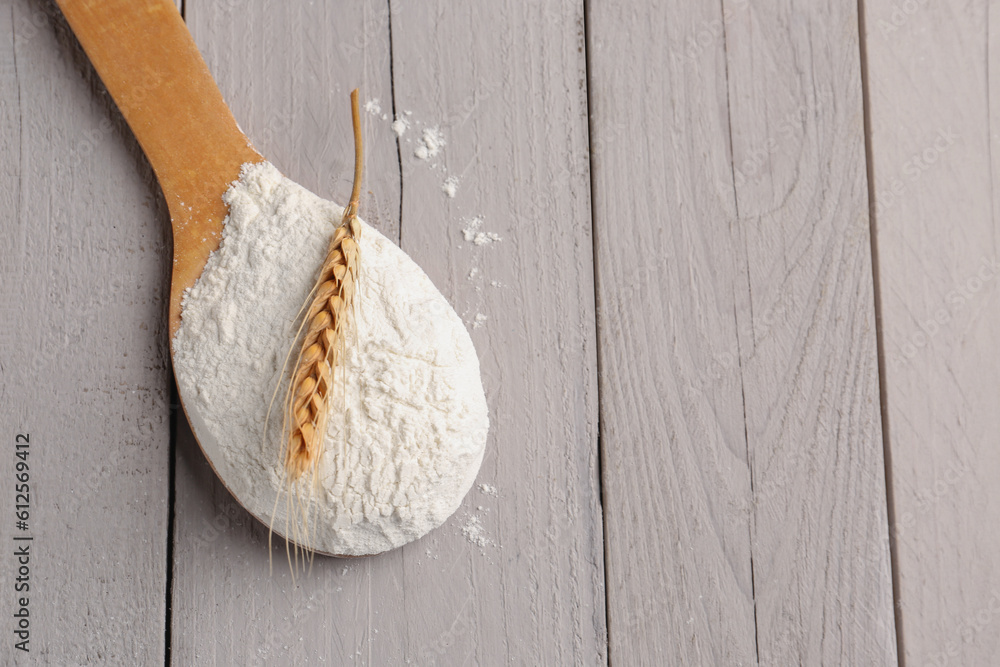 Wooden spoon with flour and wheat ear on grey wooden background