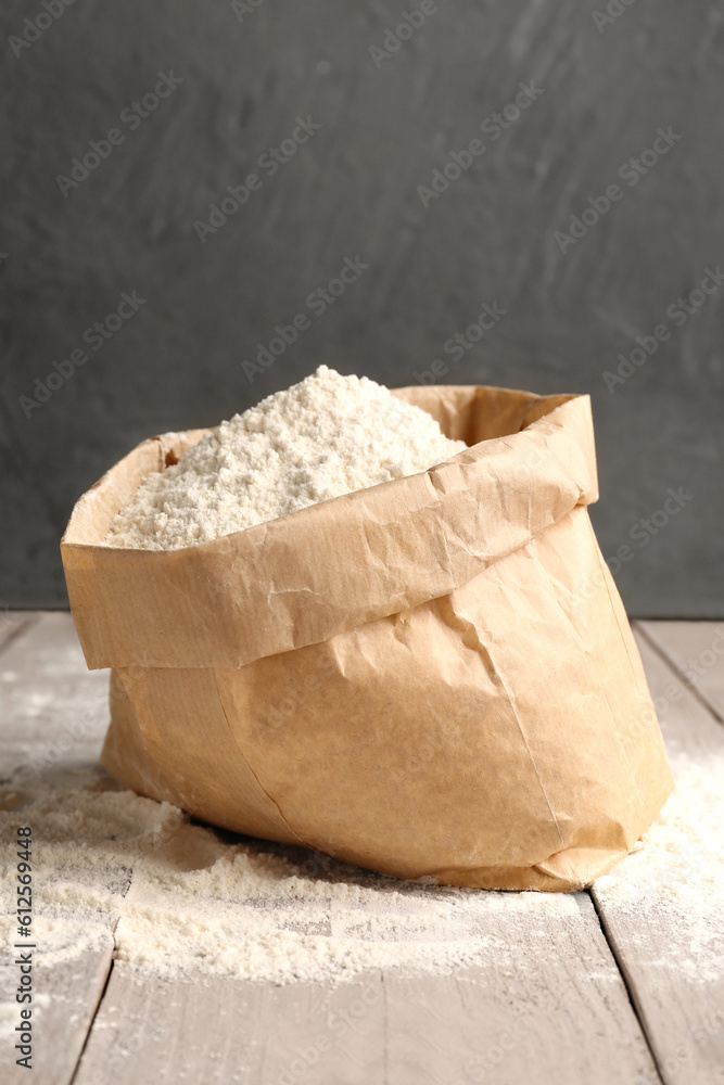 Paper bag with wheat flour on grey wooden table near wall