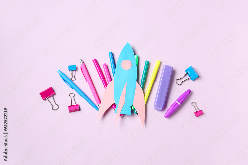 Paper rocket with different stationery on lilac background