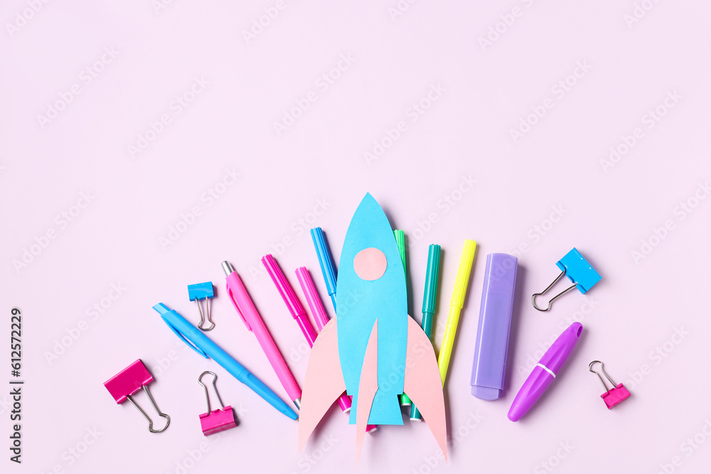 Paper rocket with different stationery on lilac background