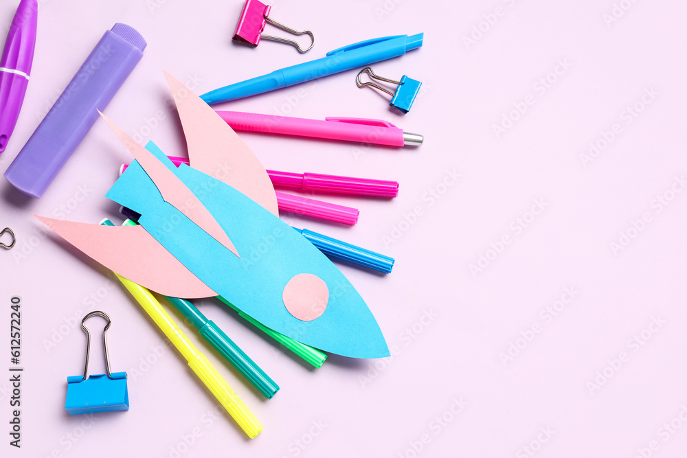 Paper rocket with different stationery on lilac background