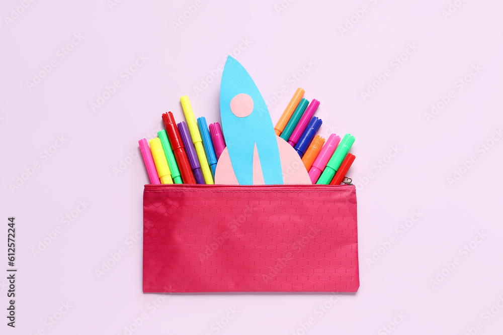 Paper rocket with pencil case and colorful markers on lilac background