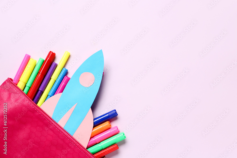 Paper rocket with pencil case and colorful markers on lilac background