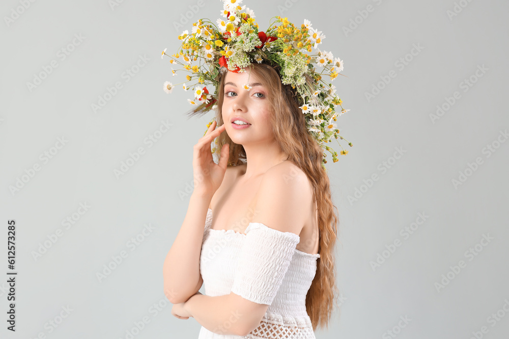 Beautiful young woman in flower wreath on light background. Summer solstice