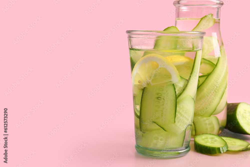 Glass and bottle of infused water with cucumber slices on pink background