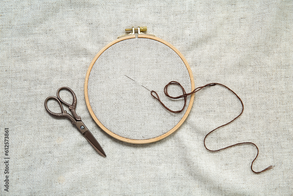 Wooden embroidery hoop with scissors, needle and canvas as background