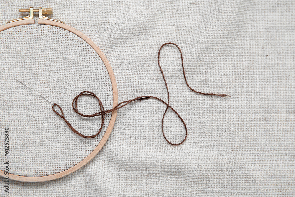 Wooden embroidery hoop with needle and canvas as background