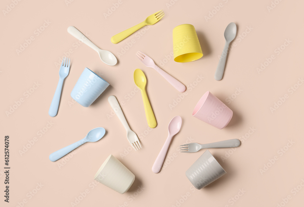 Different cups with cutlery for baby on pale pink background