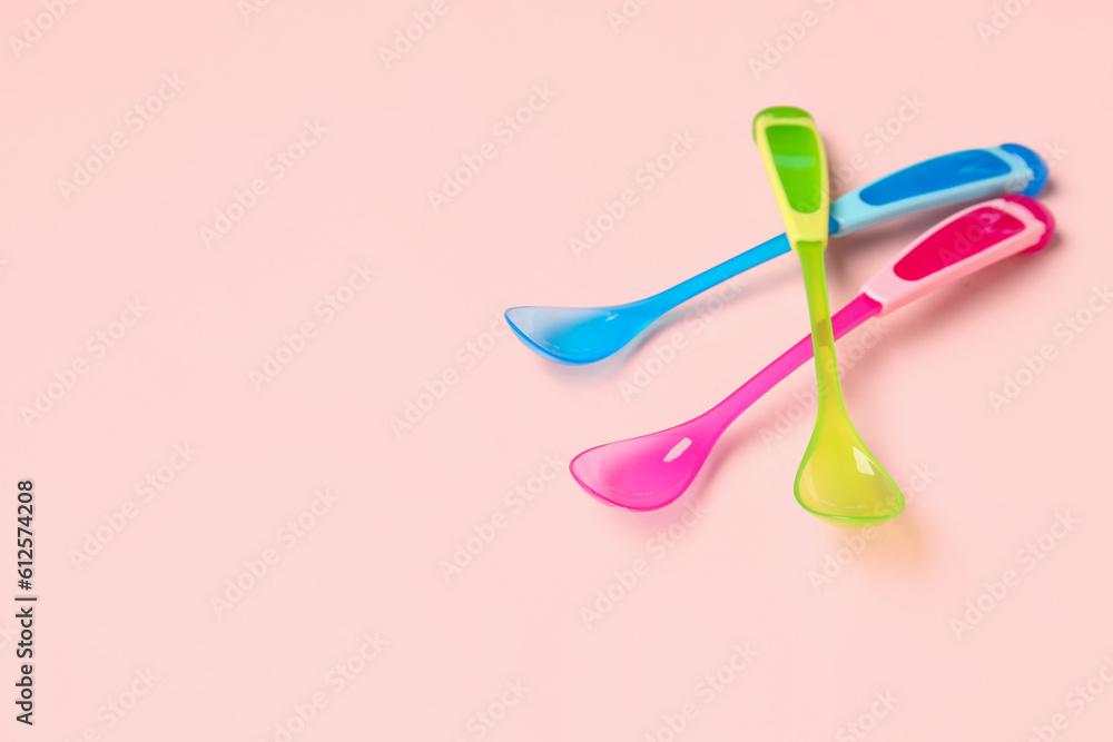 Different colorful spoons for baby on pink background