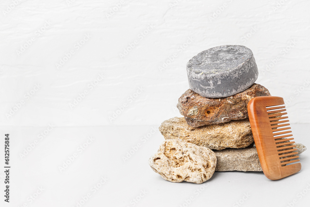 Grey solid shampoo bar with stones and comb on table near white wall