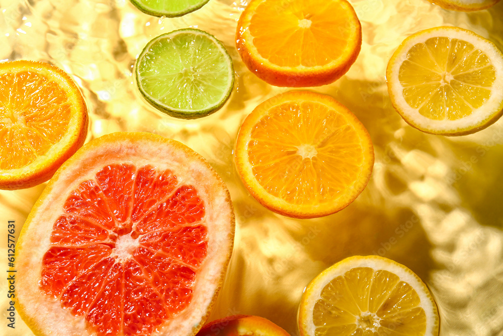 Different citrus fruit slices in water on yellow background