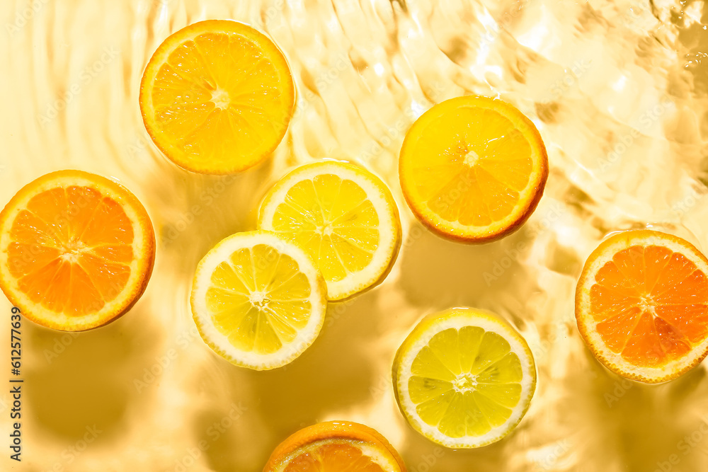 Slices of fresh orange and lemon in water on yellow background