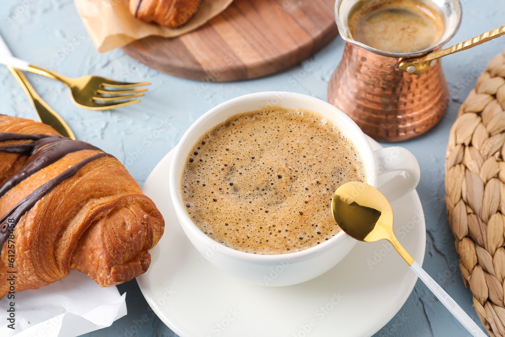 Cup of delicious espresso with jezve and croissant on blue background