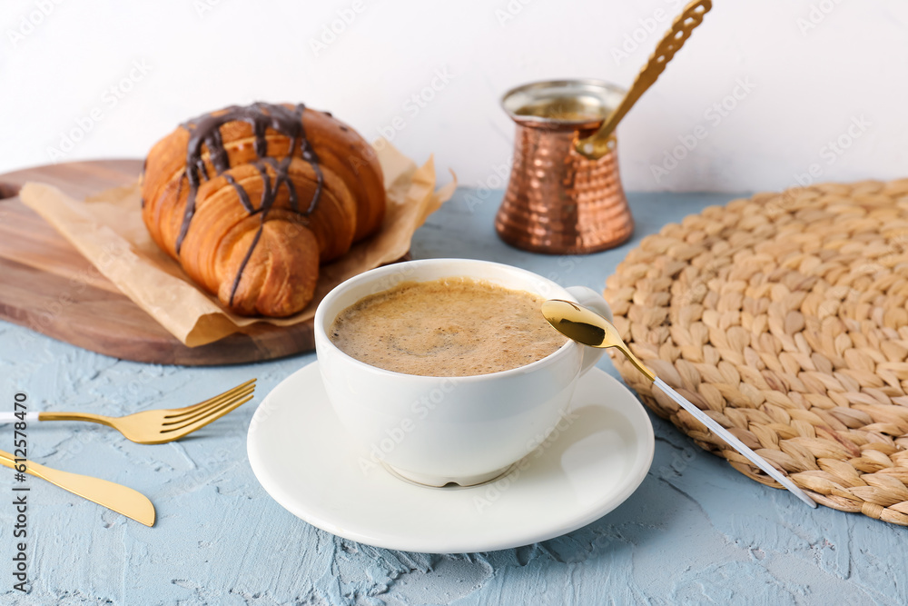 Cup of delicious espresso with jezve and croissant on blue background