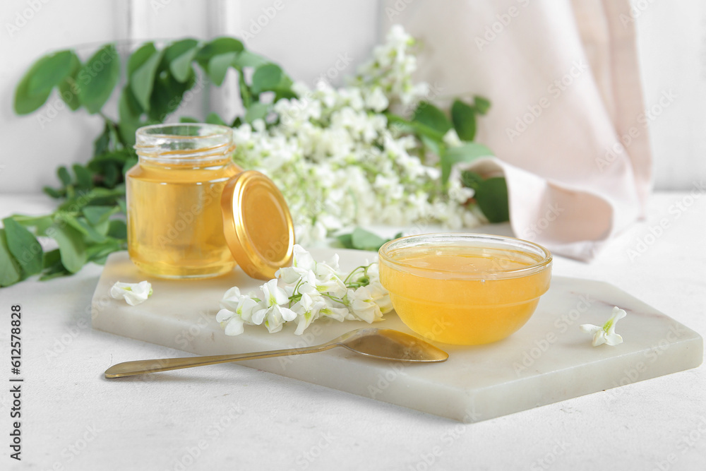 Jar and bowl of honey with flowers of acacia on light background, closeup