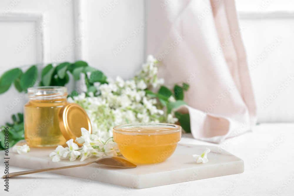 Jar and bowl of honey with flowers of acacia on light background