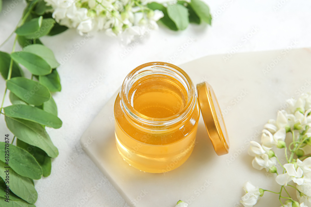 Jar of honey with flowers of acacia on light background, closeup