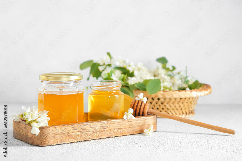 Jars of honey with flowers of acacia on light background