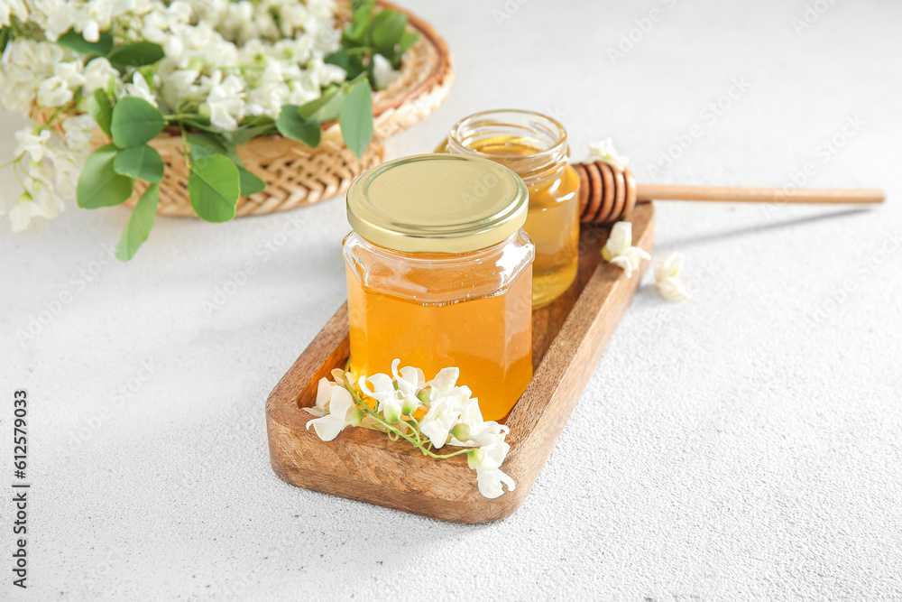 Jars of honey with flowers of acacia on light background, closeup