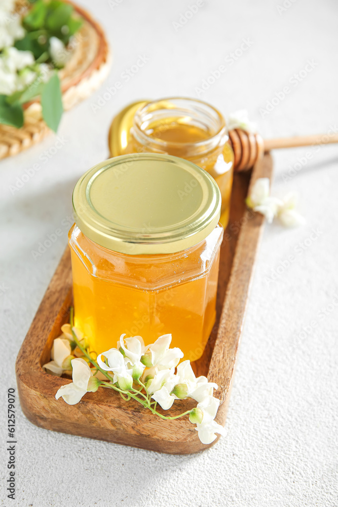 Jars of honey with flowers of acacia on light background, closeup