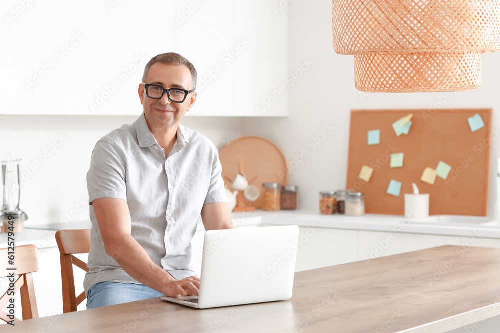 Mature man with eyeglasses using laptop in kitchen