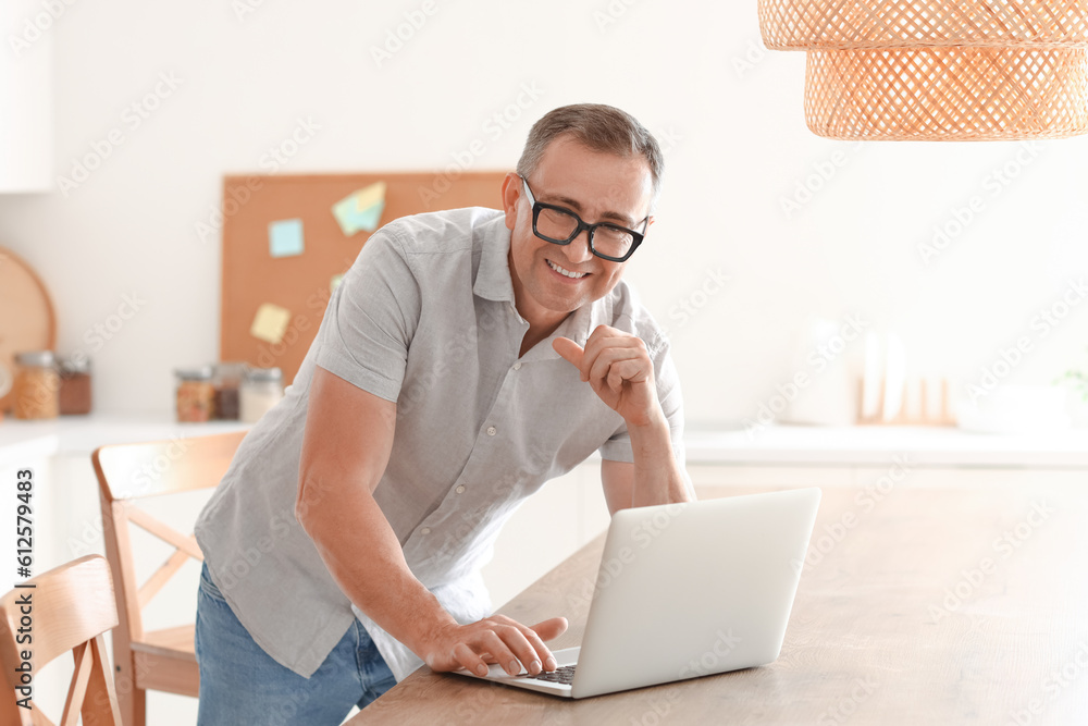 Mature man with eyeglasses using laptop in kitchen