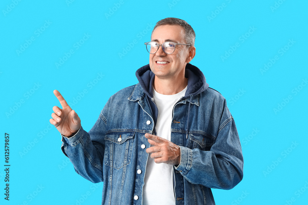 Mature man in eyeglasses pointing at something on blue background