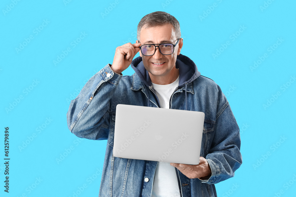 Mature man in eyeglasses with laptop on blue background