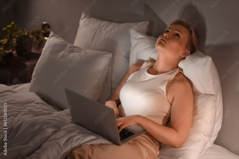 Sleepy young woman using laptop in bed at night