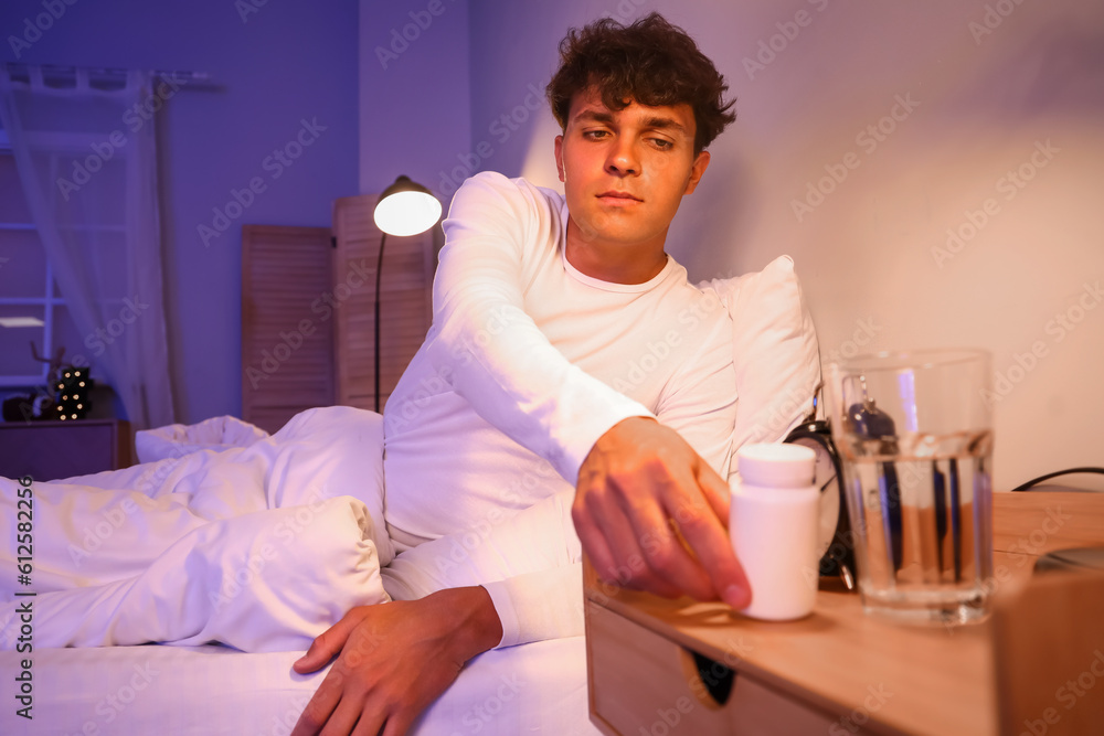 Young man taking pill bottle in bedroom at night