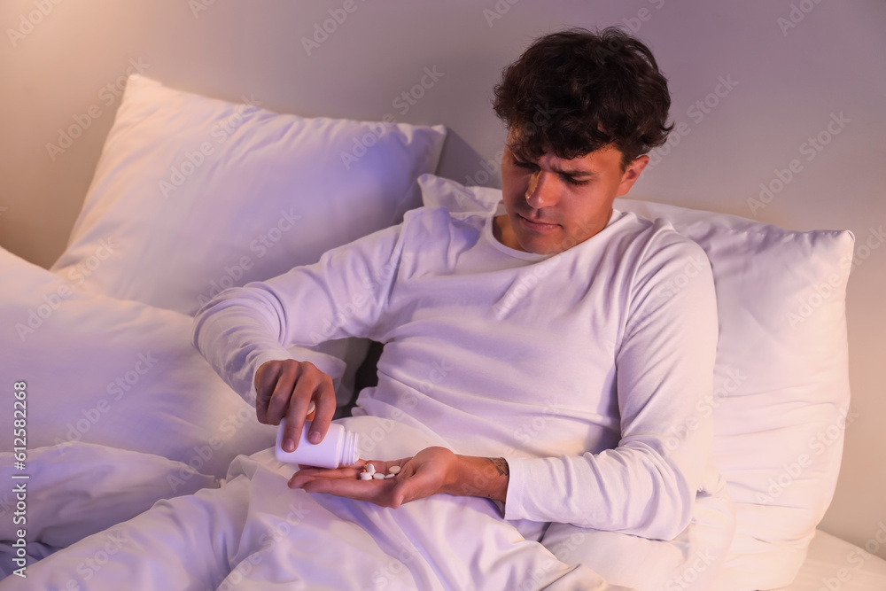 Young man taking pills before sleep in bed at night