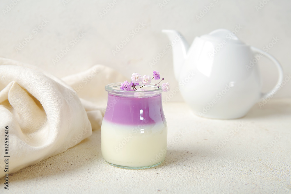 Glass of panna cotta with beautiful gypsophila flowers and teapot on white table