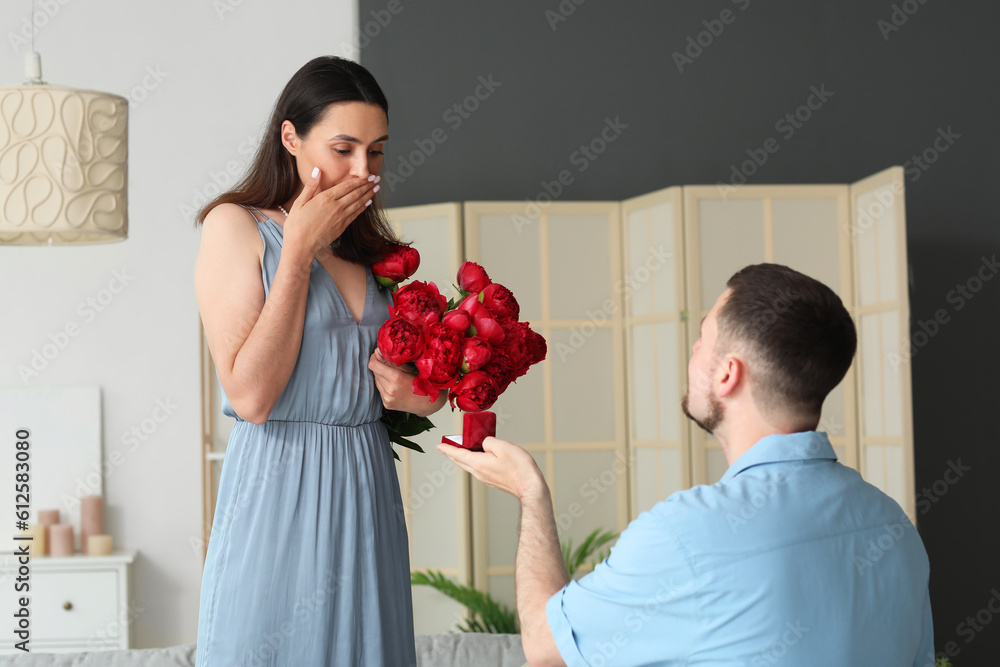 Young man proposing to his girlfriend with flowers at home