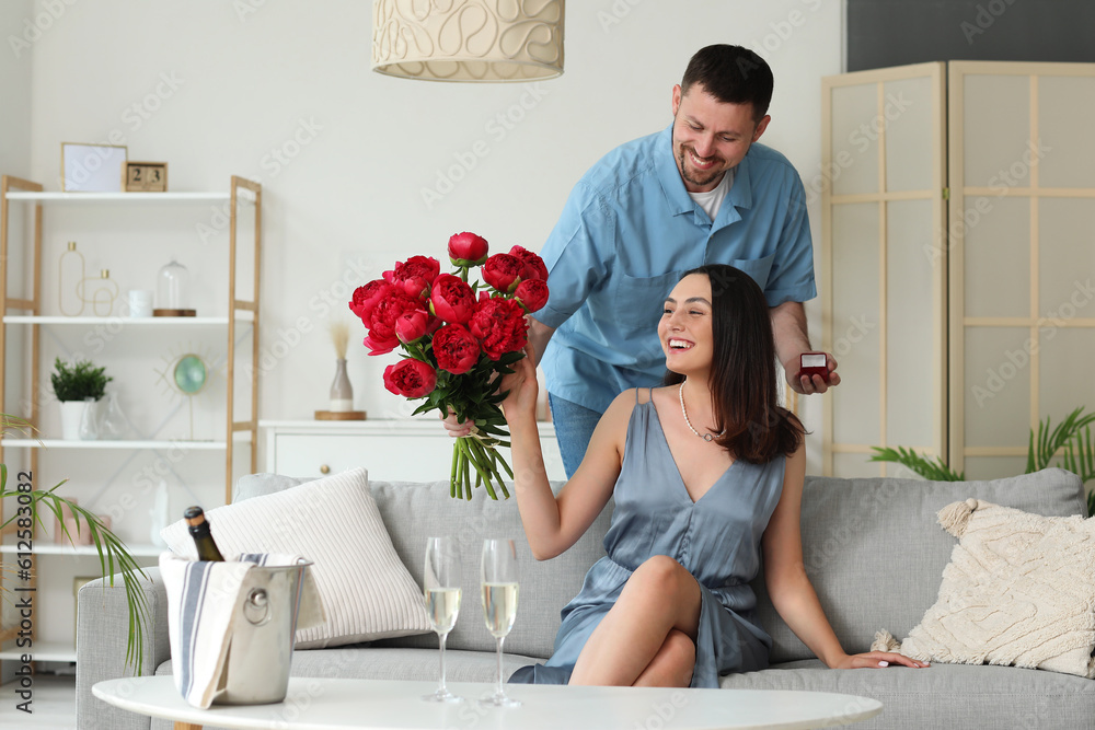 Young man with flowers proposing to his girlfriend at home