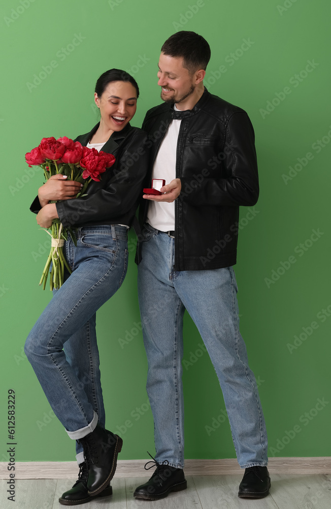 Young man proposing to his girlfriend near green wall