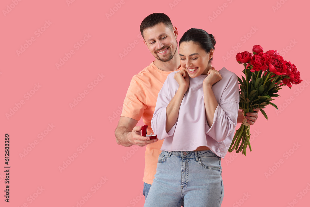 Young man with flowers proposing to his girlfriend on pink background