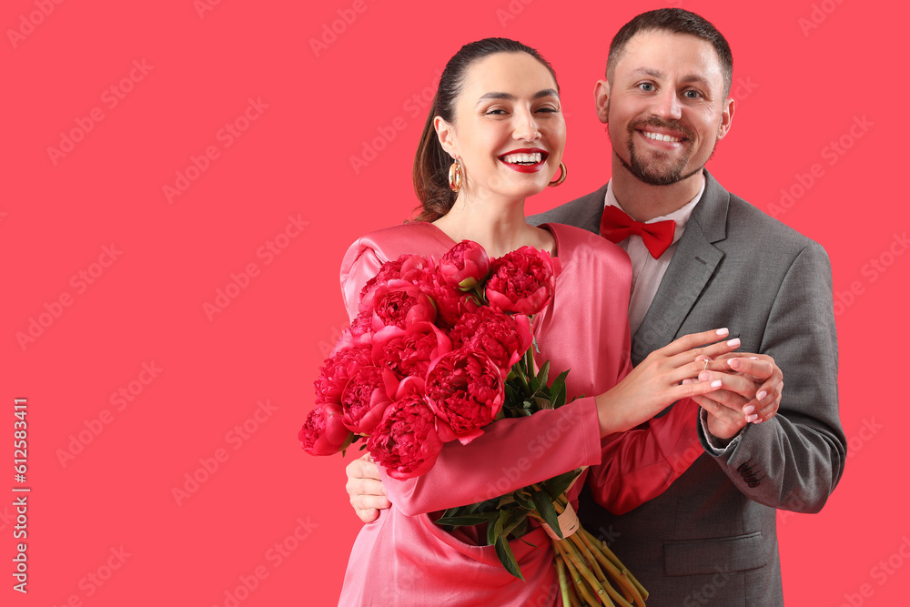 Young man putting engagement ring onto his girlfriends finger on red background