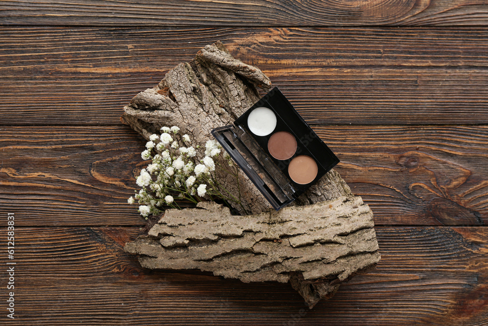 Palette of eyeshadows, tree bark and gypsophila flowers on wooden background