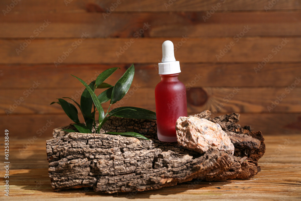 Bottle of essential oil, tree bark and plant leaves on wooden background