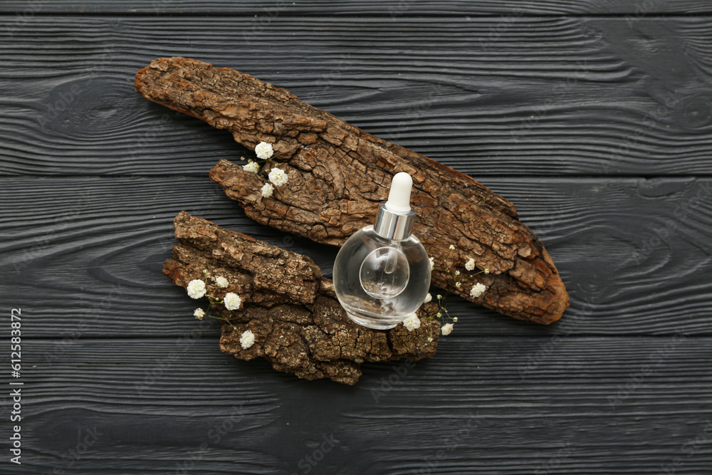 Bottle of essential oil, tree bark and gypsophila flowers on dark wooden background