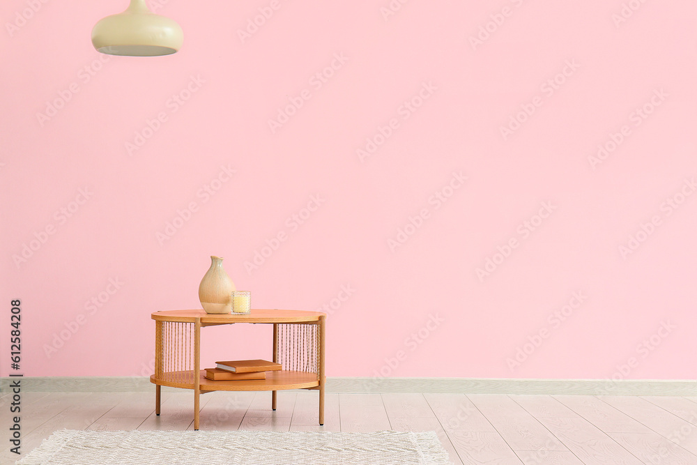 Wooden coffee table with vase, candle and books near pink wall