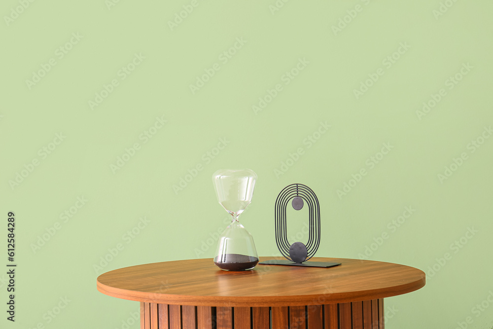 Wooden coffee table with hourglass and decorative figure near green wall