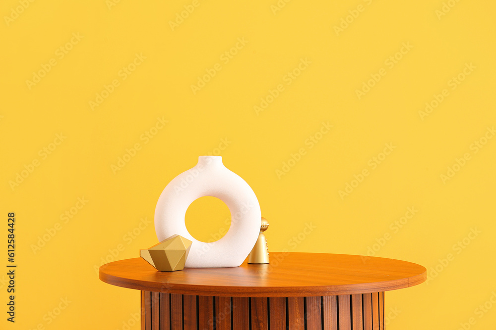 Wooden coffee table with empty vase and decorative figures near orange wall